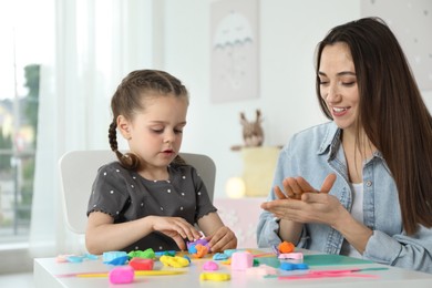 Photo of Smiling mother and her daughter sculpting with play dough at table indoors