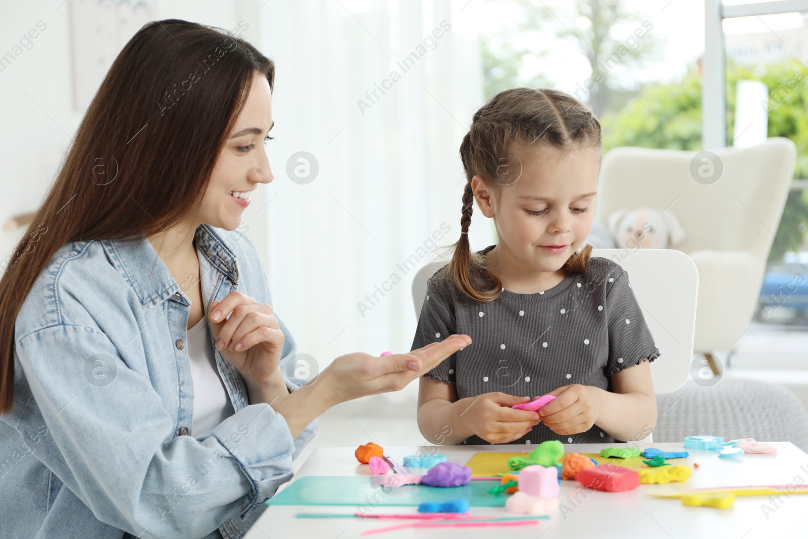 Photo of Smiling mother and her daughter sculpting with play dough at table indoors