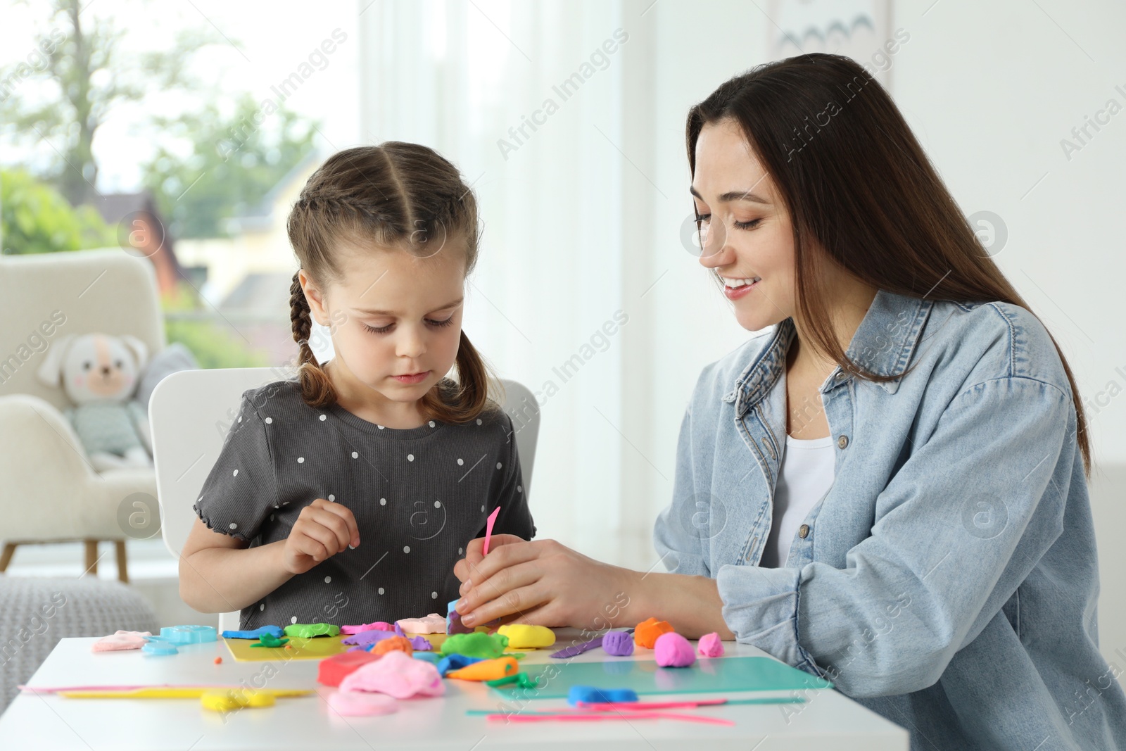 Photo of Smiling mother and her daughter sculpting with play dough at table indoors