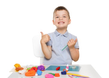 Smiling boy showing thumbs up at table with play dough on white background