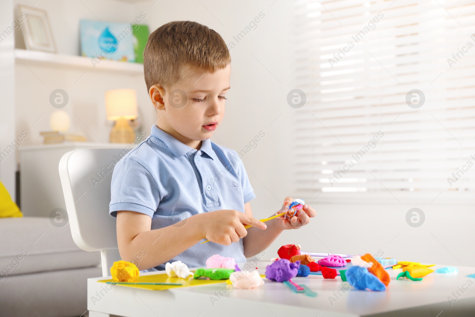 Photo of Little boy sculpting with play dough at table indoors