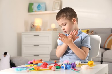 Photo of Little boy sculpting with play dough at table indoors