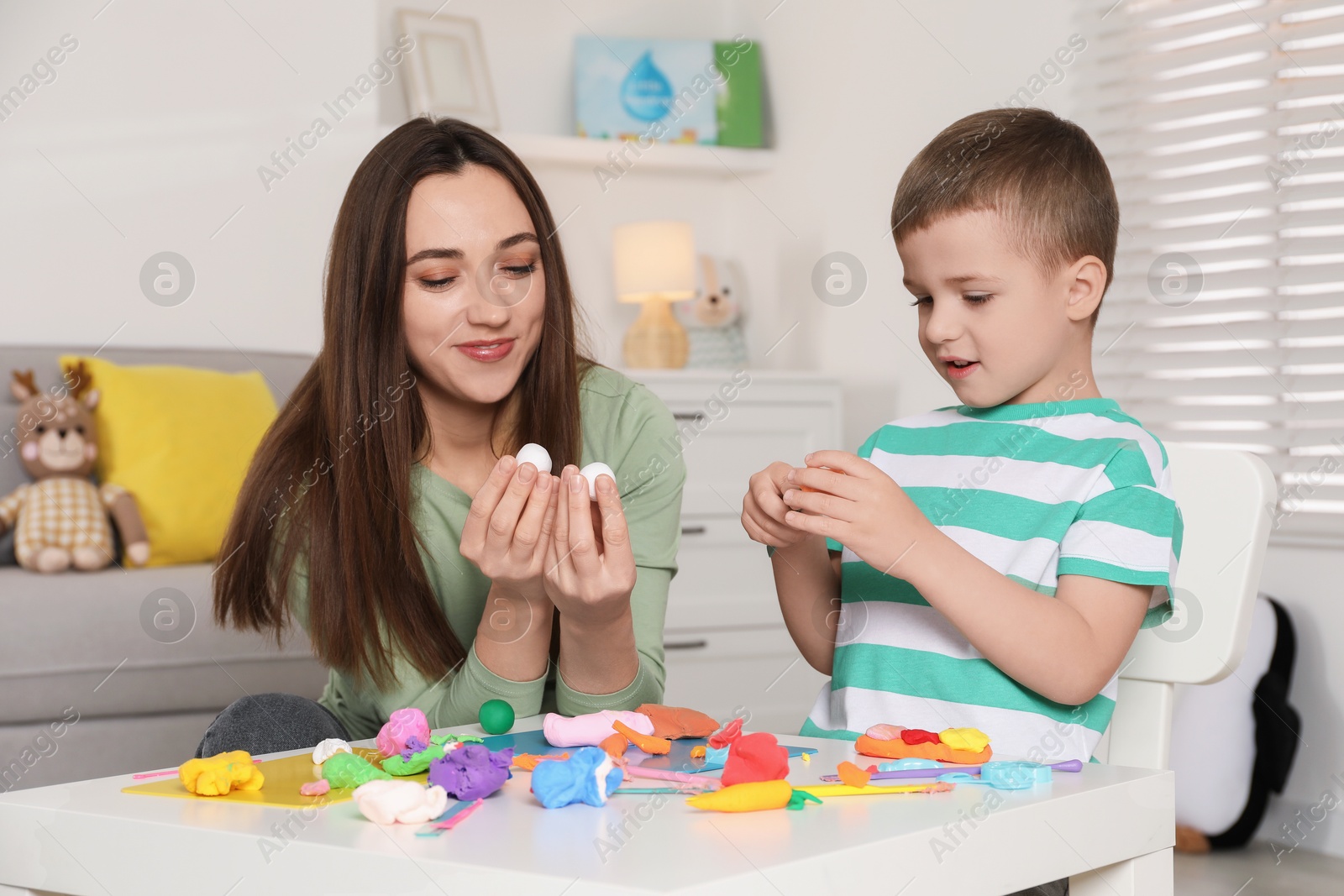 Photo of Son and mother sculpting with play dough at table indoors