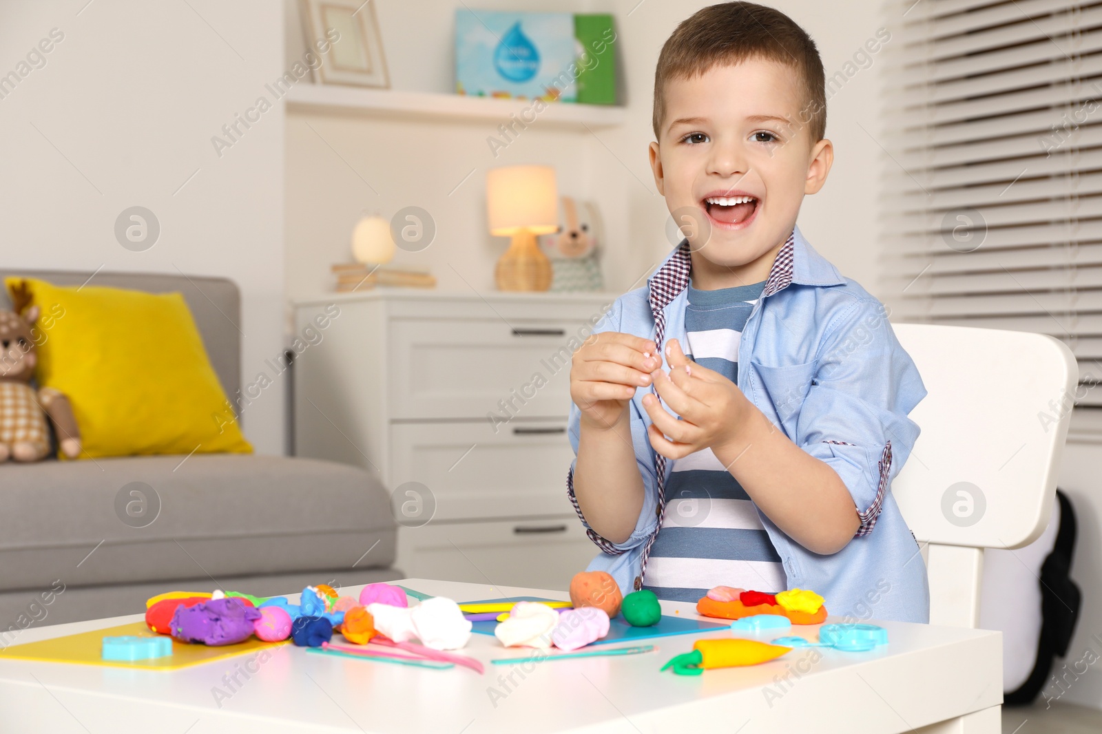 Photo of Happy boy sculpting with play dough at table in kindergarten. Space for text