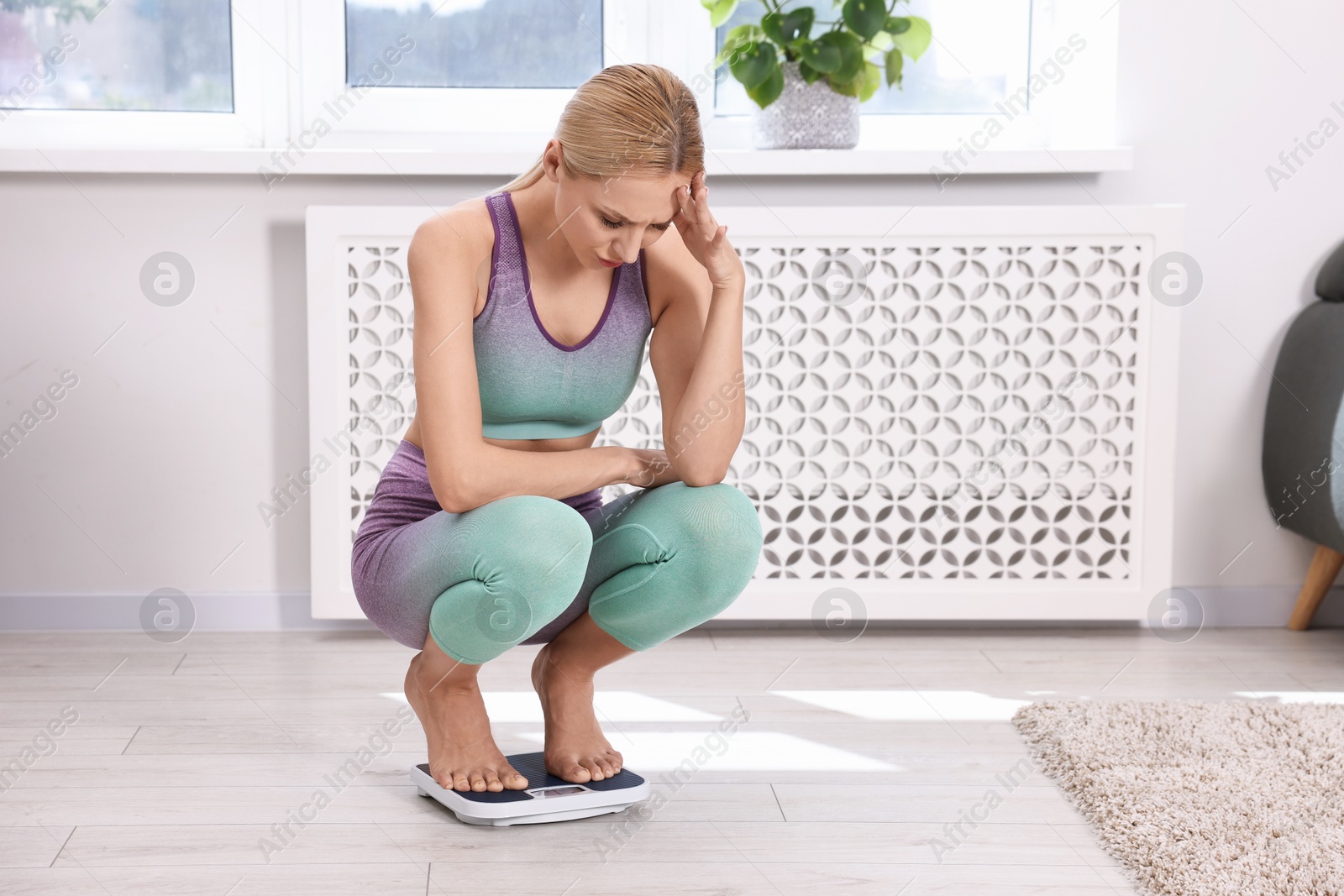 Photo of Worried woman on floor scale at home