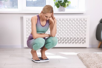 Worried woman on floor scale at home