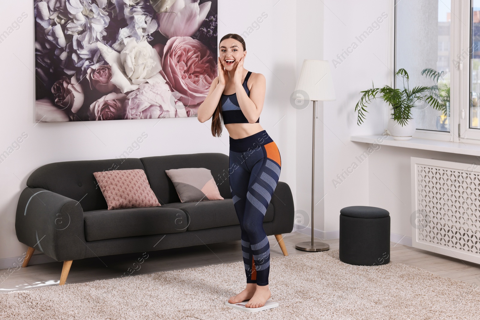 Photo of Happy woman standing on floor scale at home