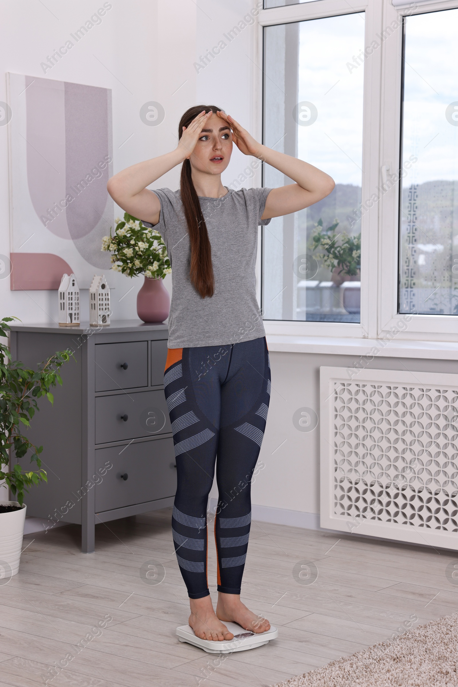 Photo of Worried woman standing on floor scale at home