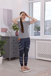 Worried woman standing on floor scale at home