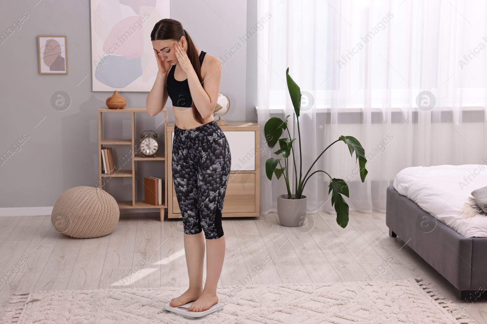 Photo of Worried woman standing on floor scale at home