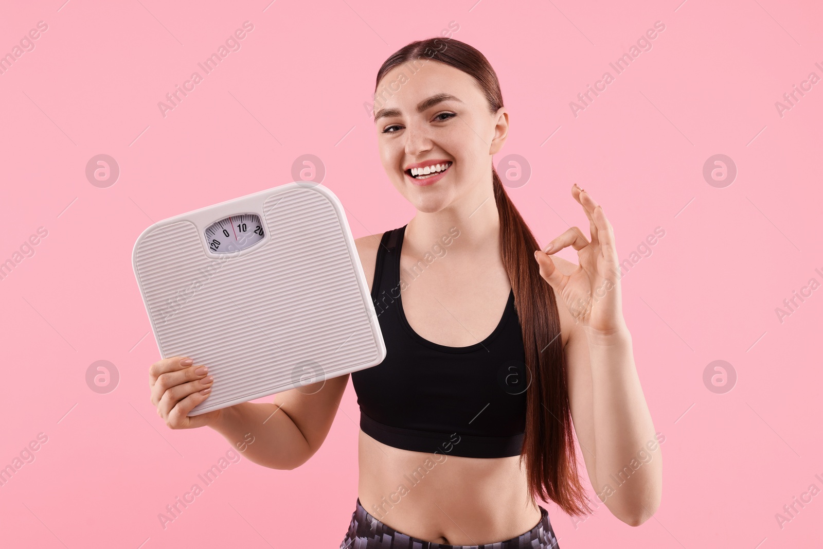 Photo of Happy woman with floor scale showing ok gesture on pink background