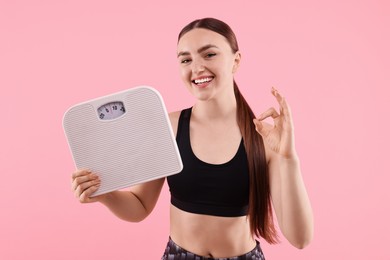 Happy woman with floor scale showing ok gesture on pink background