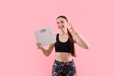 Photo of Happy woman with floor scale showing ok gesture on pink background. Space for text