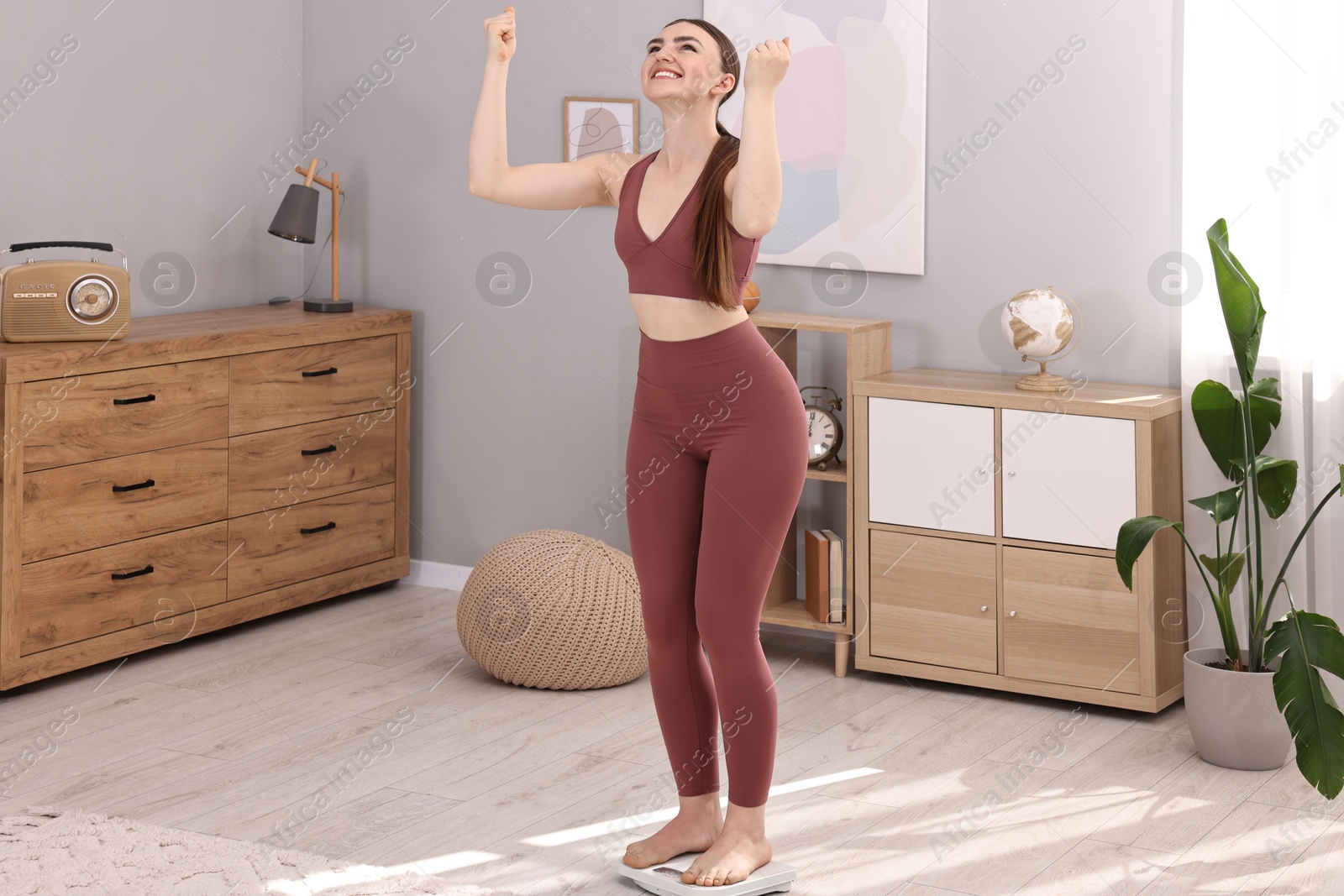 Photo of Happy woman standing on floor scale at home