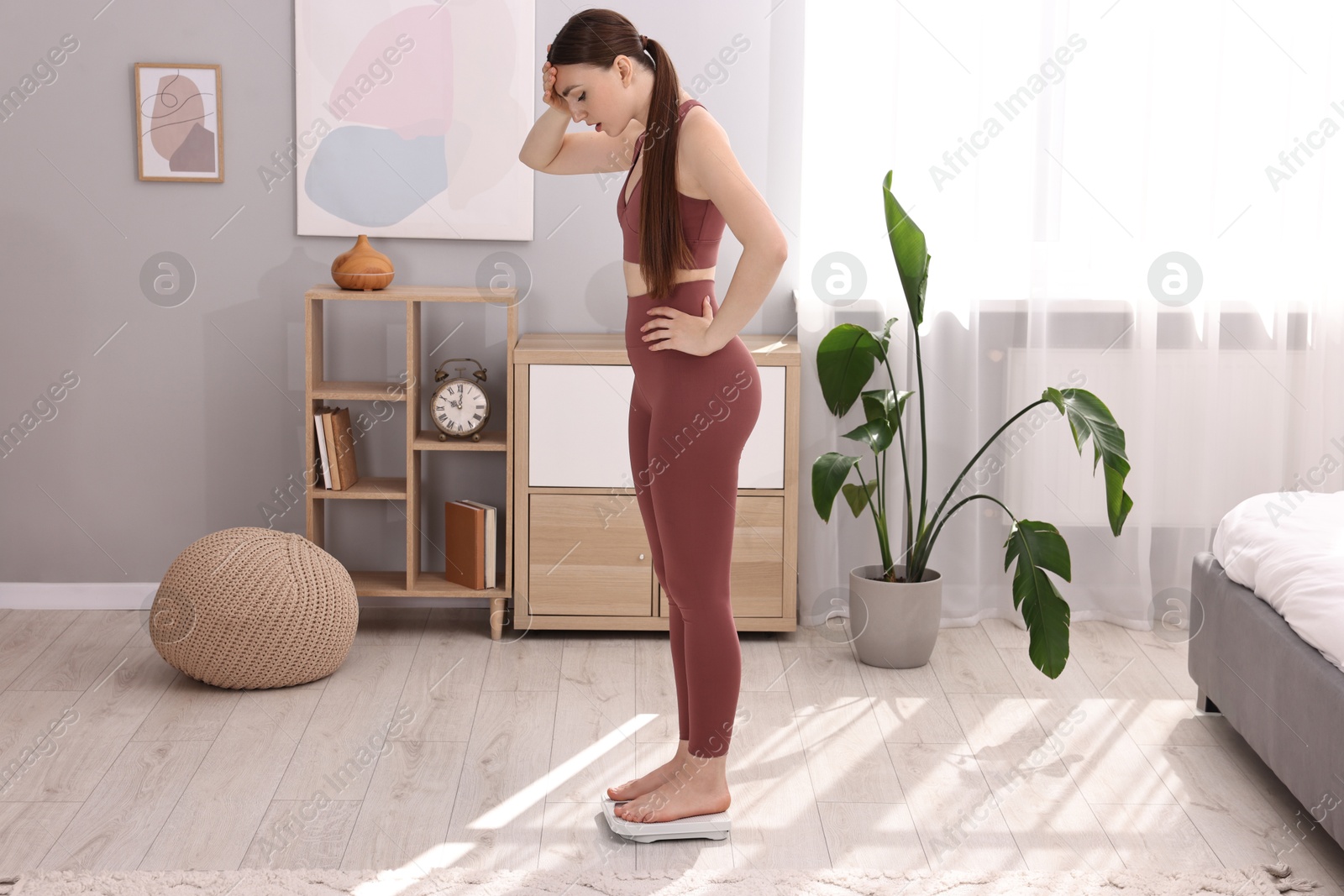 Photo of Worried woman standing on floor scale at home