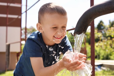 Photo of Water scarcity. Cute little boy drawing water with hands from tap outdoors