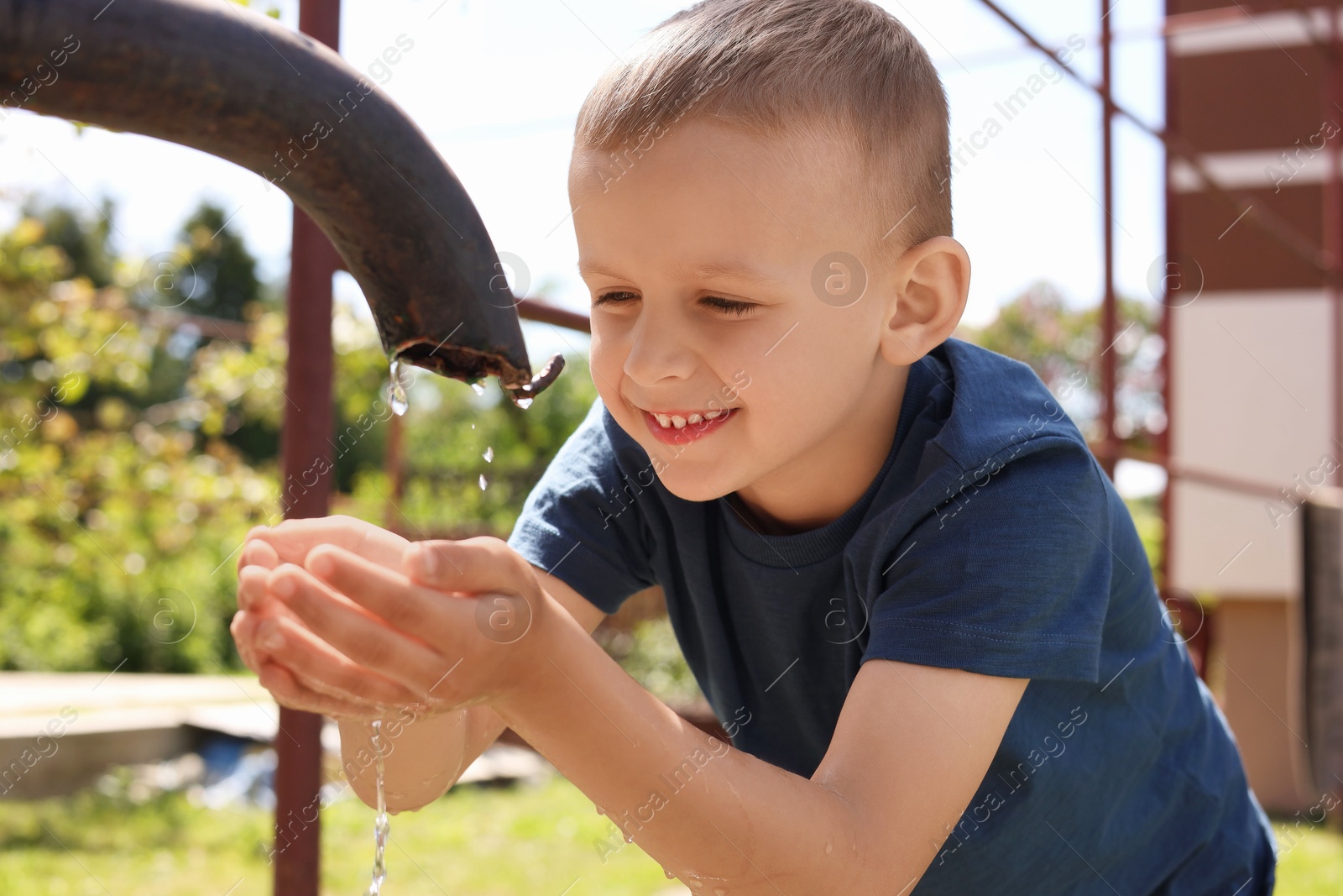 Photo of Water scarcity. Cute little boy drawing water with hands from tap outdoors