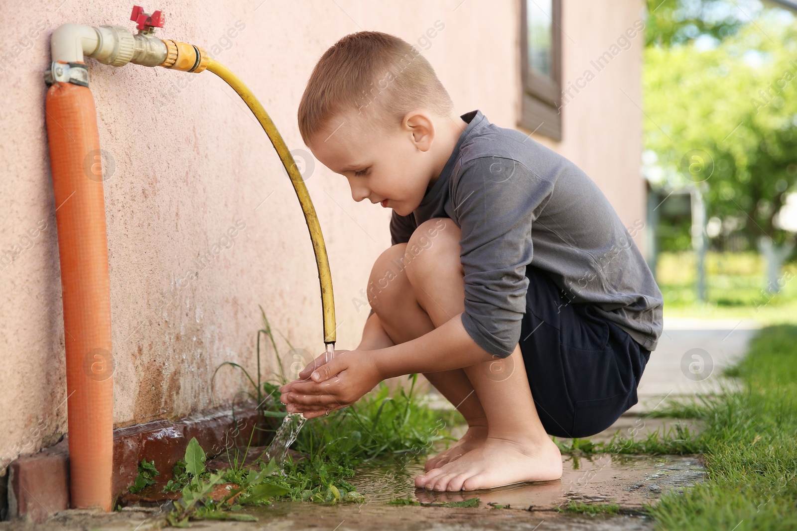 Photo of Water scarcity. Cute little boy drawing water with hands from tap outdoors