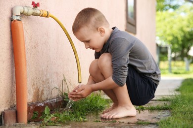 Water scarcity. Cute little boy drawing water with hands from tap outdoors