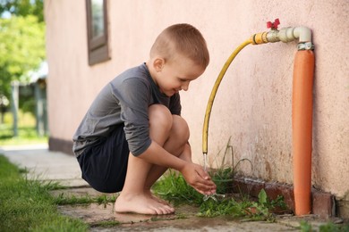 Photo of Water scarcity. Cute little boy drawing water with hands from tap outdoors