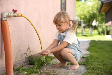 Water scarcity. Cute little girl drawing water with hands from tap outdoors