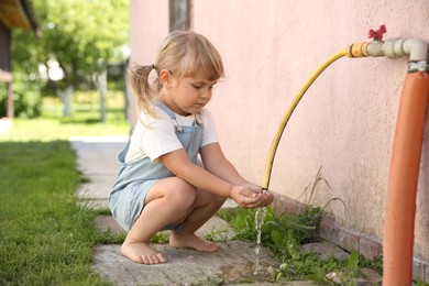 Photo of Water scarcity. Cute little girl drawing water with hands from tap outdoors