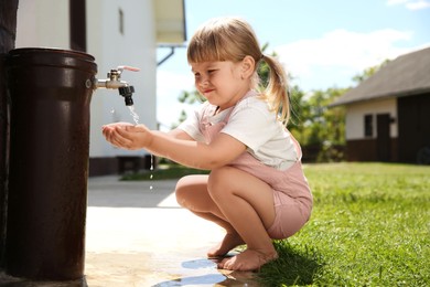 Water scarcity. Cute little girl drawing water with hands from tap outdoors