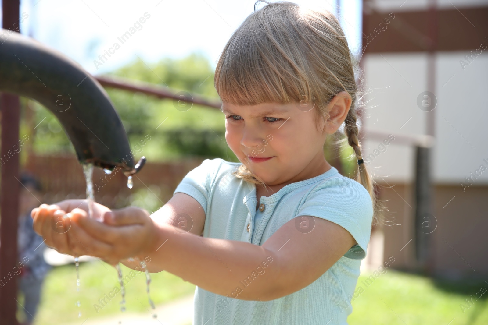 Photo of Water scarcity. Cute little girl drawing water with hands from tap outdoors