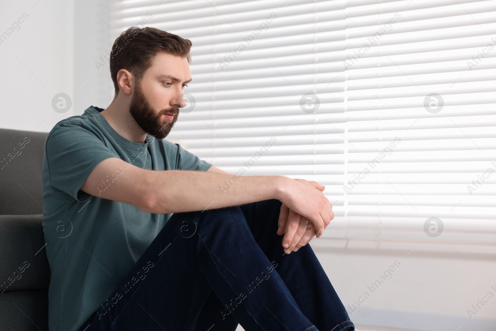 Photo of Loneliness concept. Sad man sitting on floor at home, space for text