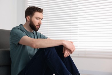 Photo of Loneliness concept. Sad man sitting on floor at home, space for text