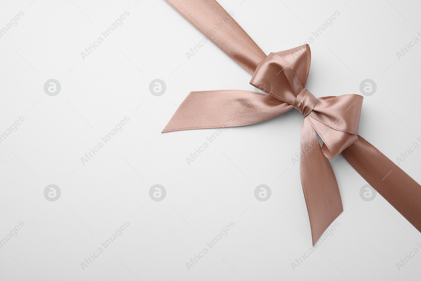 Photo of Beige satin ribbon with bow on white background, top view. Space for text