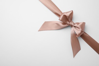 Beige satin ribbon with bow on white background, top view. Space for text