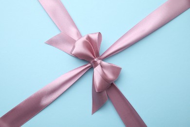 Photo of Pink satin ribbon with bow on light blue background
