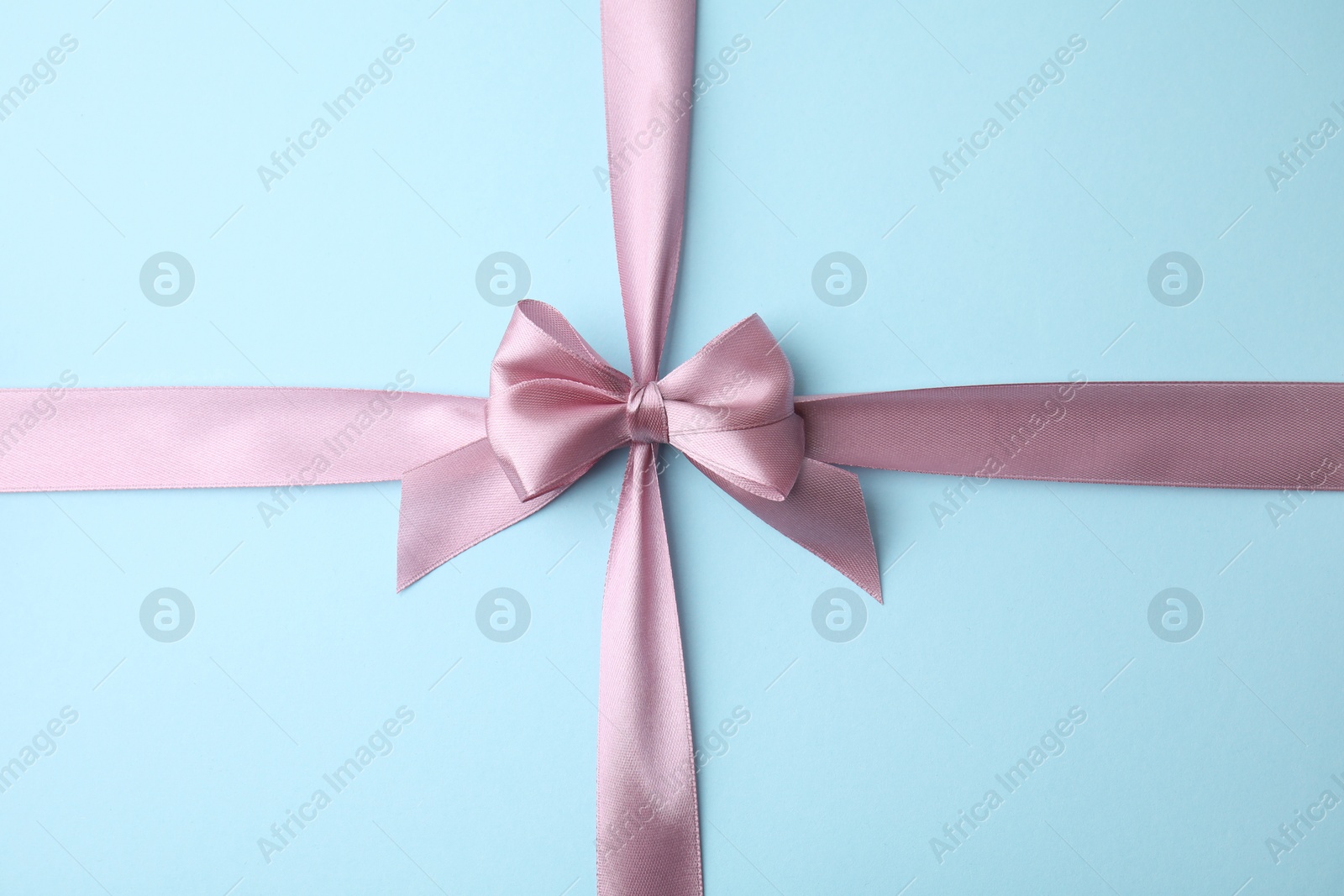 Photo of Pink satin ribbon with bow on light blue background, top view