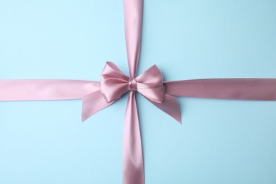 Pink satin ribbon with bow on light blue background, top view