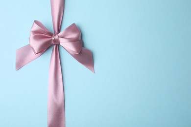 Pink satin ribbon with bow on light blue background, top view