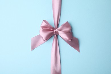 Pink satin ribbon with bow on light blue background, top view