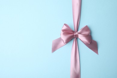 Pink satin ribbon with bow on light blue background, top view