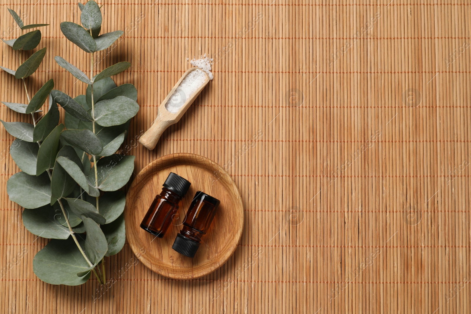 Photo of Aromatherapy products. Bottles of essential oil, sea salt and eucalyptus branches on bamboo mat, flat lay. Space for text