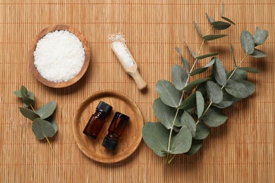 Photo of Aromatherapy products. Bottles of essential oil, sea salt and eucalyptus branches on bamboo mat, flat lay