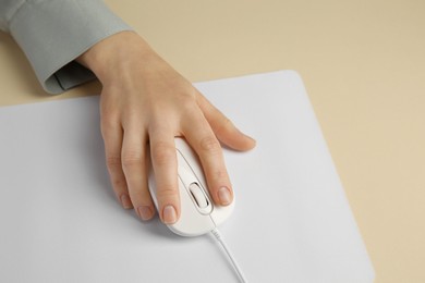 Photo of Woman using modern wired computer mouse on beige background, closeup