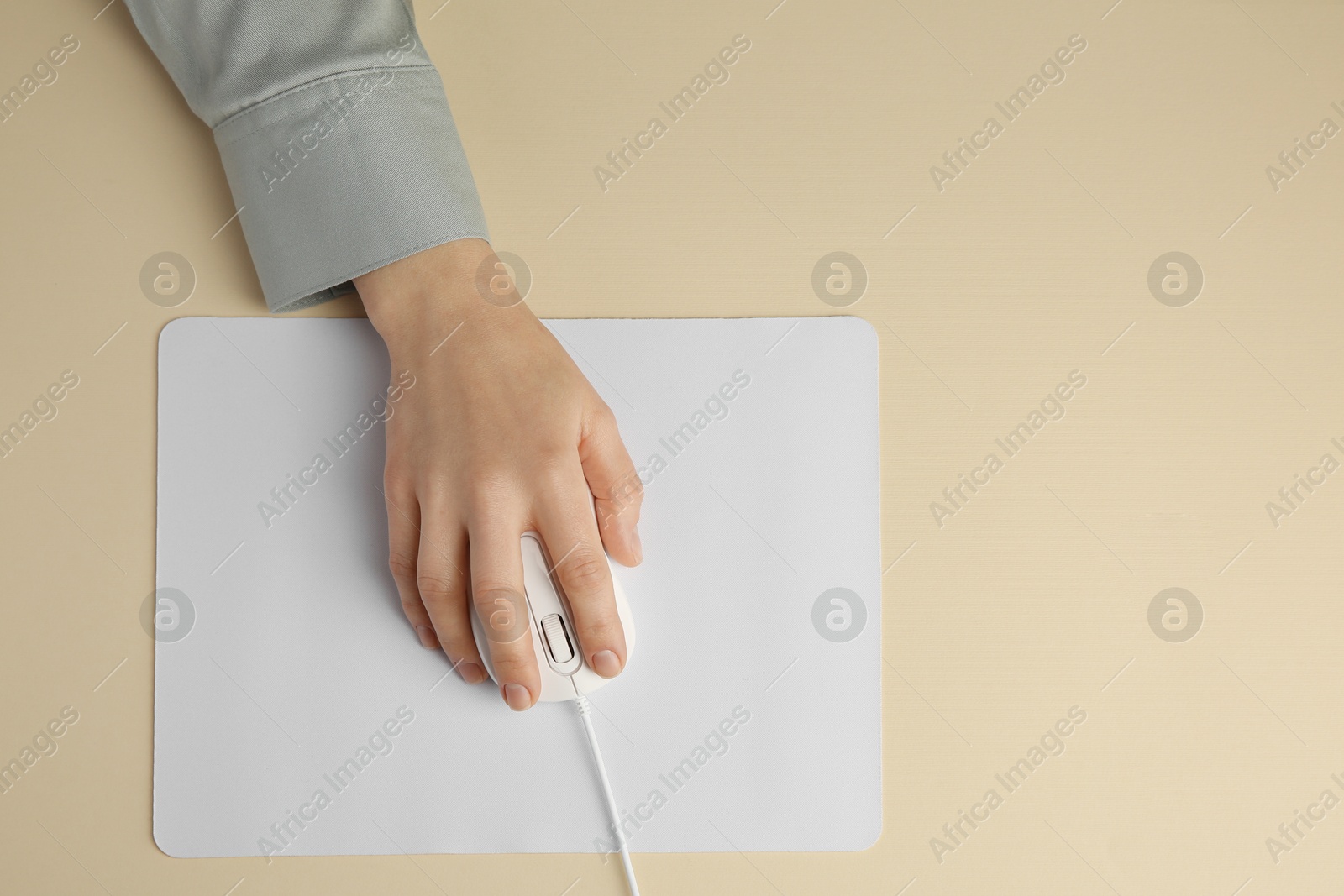 Photo of Woman using modern wired computer mouse on beige background, top view. Space for text