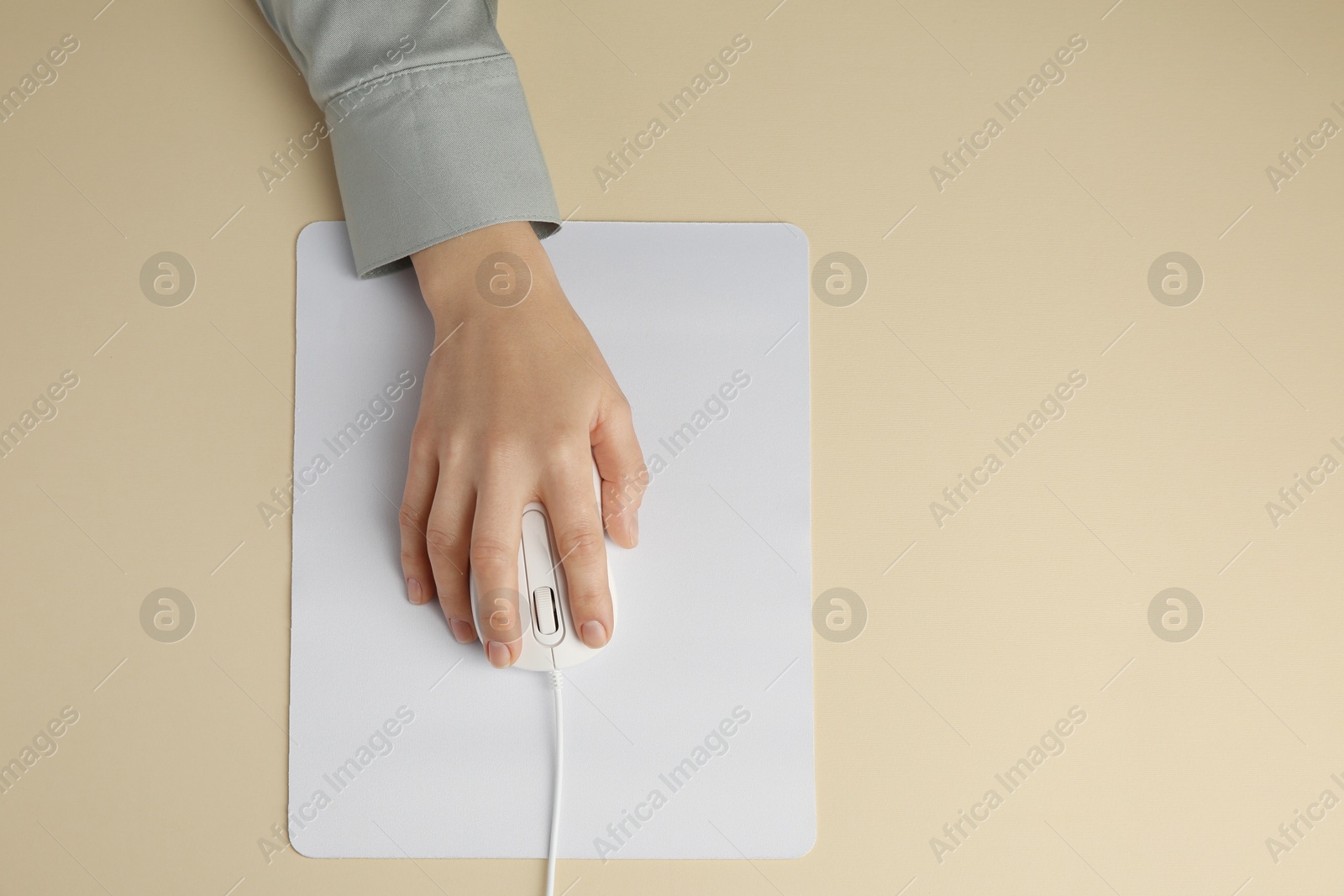 Photo of Woman using modern wired computer mouse on beige background, top view. Space for text