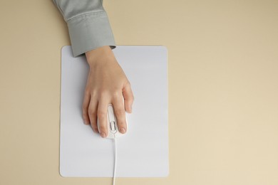 Woman using modern wired computer mouse on beige background, top view. Space for text