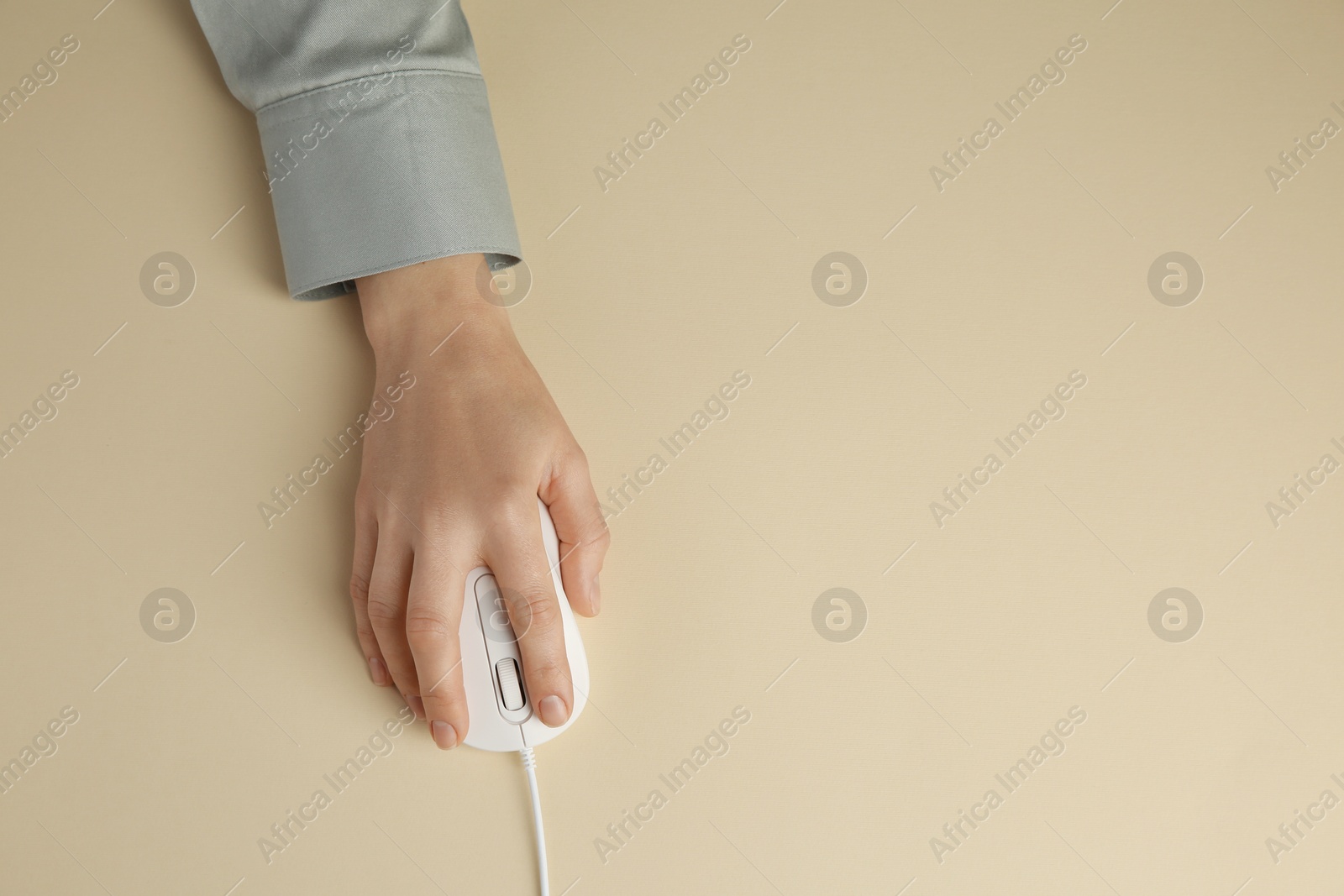 Photo of Woman using modern wired computer mouse on beige background, top view. Space for text