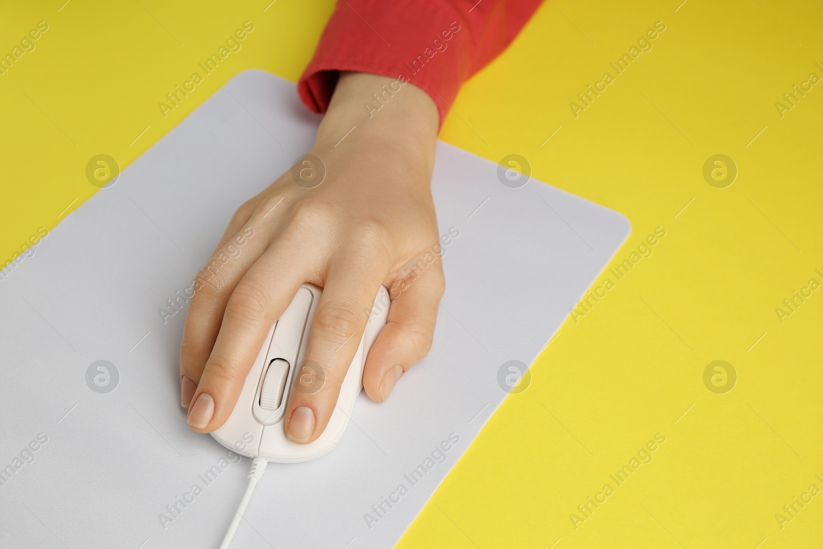 Photo of Woman using modern wired computer mouse on yellow background, closeup