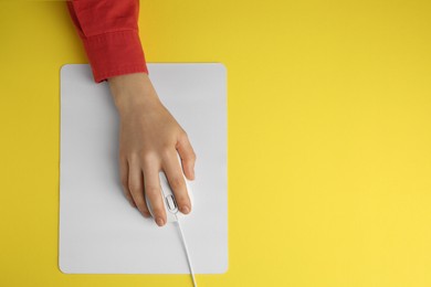 Photo of Woman using modern wired computer mouse on yellow background, top view. Space for text