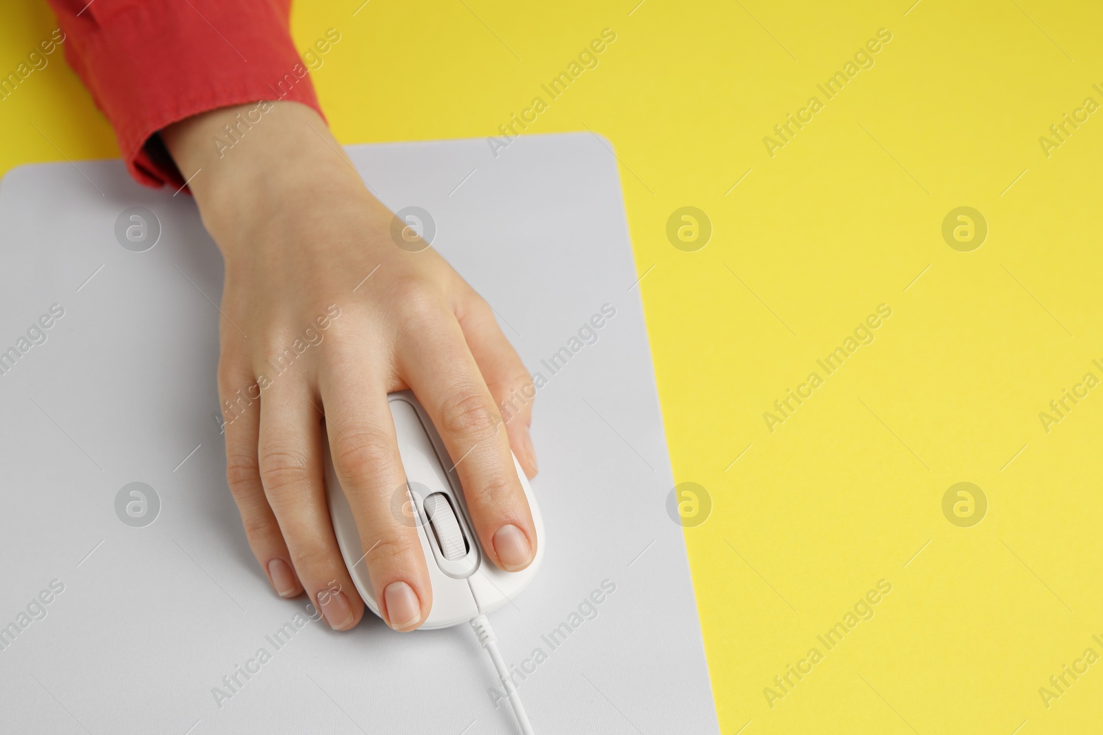 Photo of Woman using modern wired computer mouse on yellow background, closeup. Space for text