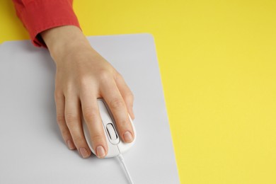 Woman using modern wired computer mouse on yellow background, closeup. Space for text