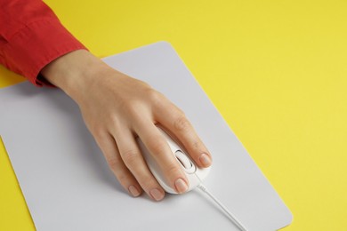 Photo of Woman using modern wired computer mouse on yellow background, closeup